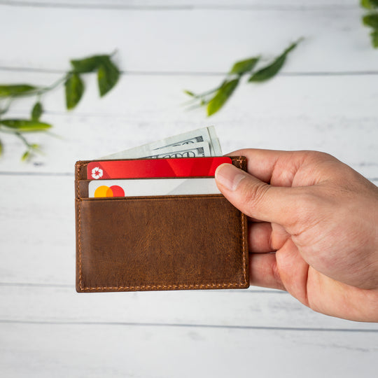 Hand holding a brown leather wallet with cards and money against a light background